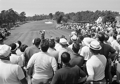 B&W photo circa mid-1960s showing gallery behind tee at PGA golf tournament watching a player tee off