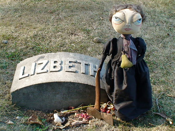 gag photo showing a little Lizzie Borden doll with an ax standing next to Lizzie Borden's grave in Fall River, Massachusetts
