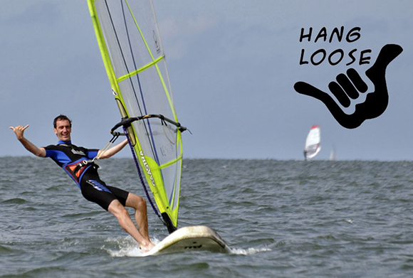 photo of man in wetsuit windsurfing and giving traditional Hawaiian hand signal for hang loose