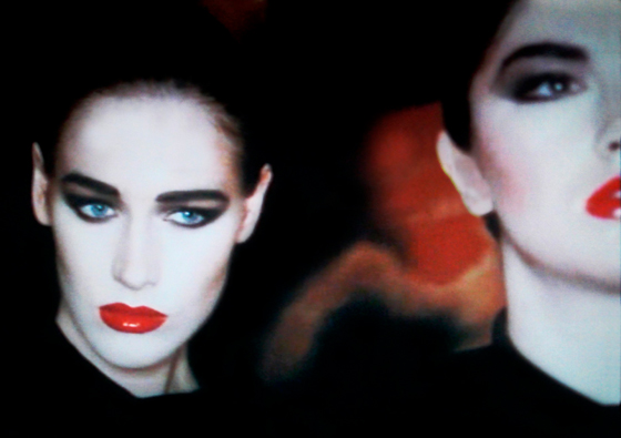 Still photo from Robert Palmer Addicted To Love video showing girl with white face, dark eye mascara and makeup, and very red lips